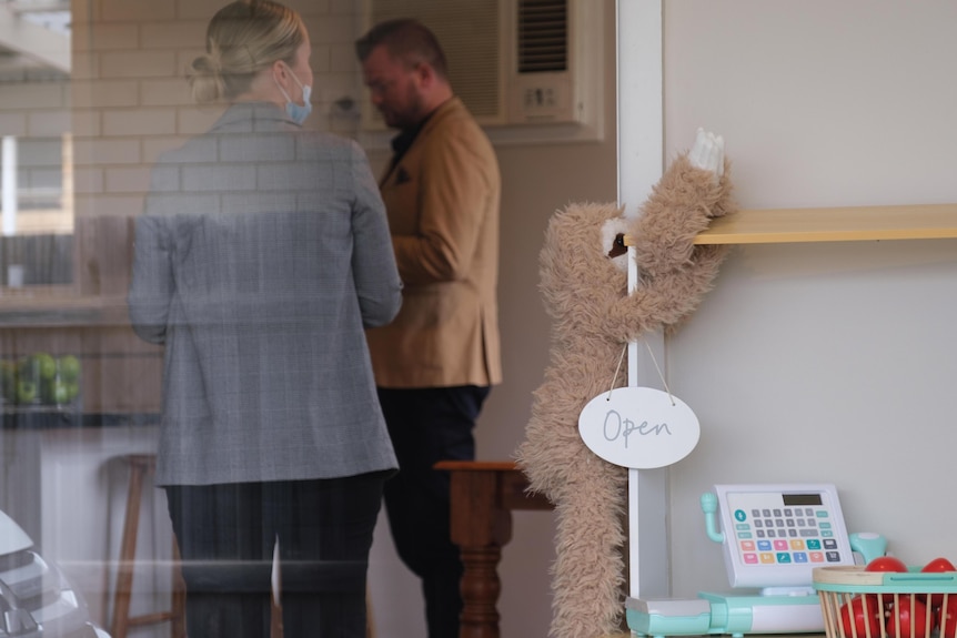 Nathan and Oliver stand inside the living room and kitchen.