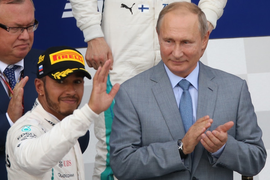F1 driver Lewis Hamilton waves to a crowd as Russian President Vladimir Putin applauds him at the Russian Grand Prix.