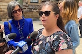 A lady speaking to journalists outside of a court.