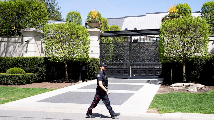 A police officer walks past a gated mansion.