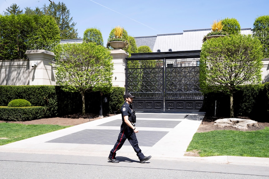 A police officer walks past a gated mansion.