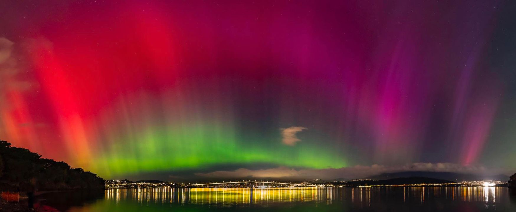 Hobart's Tasman Bridge at night, with the sky lit up in green, red and pink from Aurora Australis