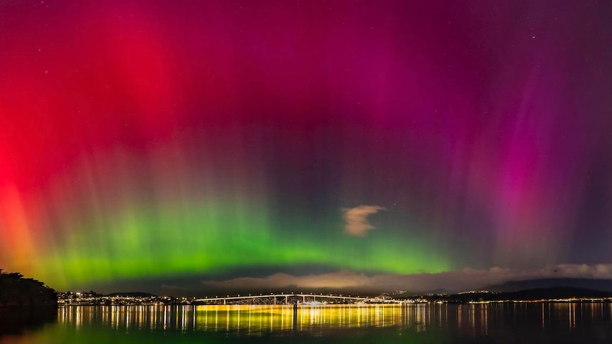Hobart's Tasman Bridge at night, with the sky lit up in green, red and pink from Aurora Australis