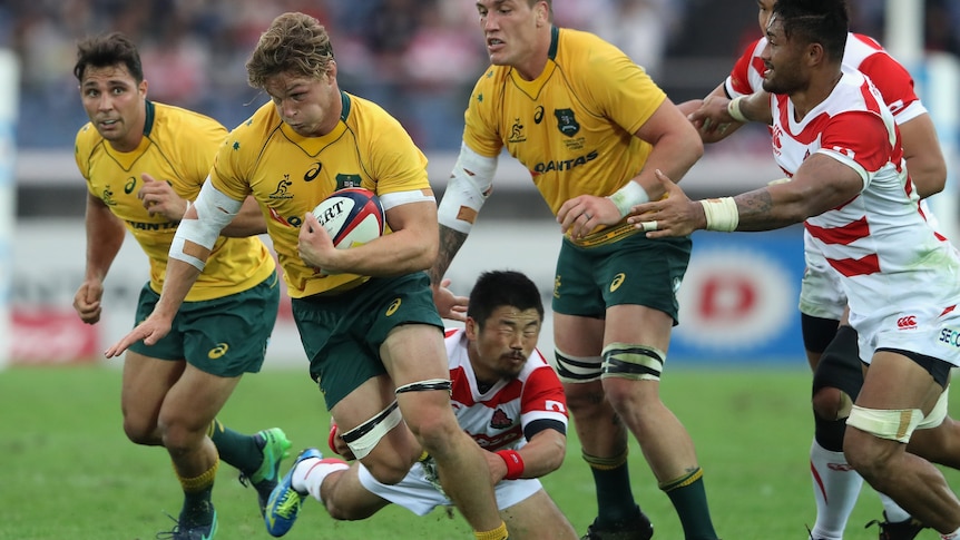 An Australian rugby union international puffs his cheeks out as he tries to break a tackle in a match against Japan.