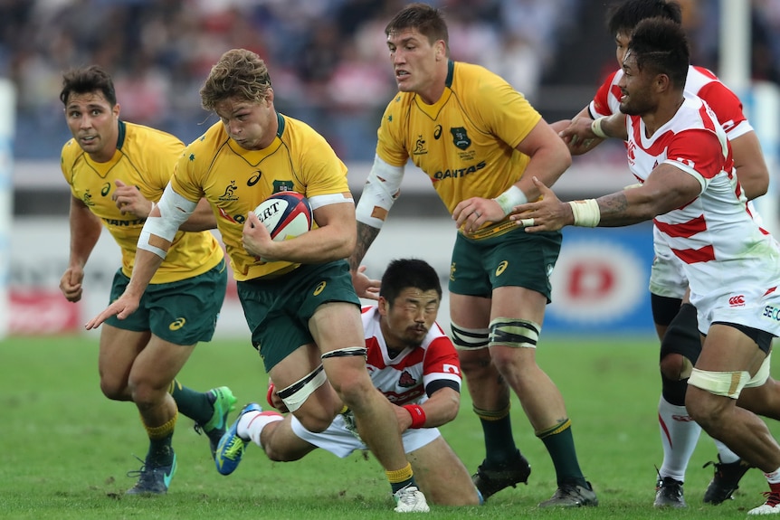 An Australian rugby union international puffs his cheeks out as he tries to break a tackle in a match against Japan.