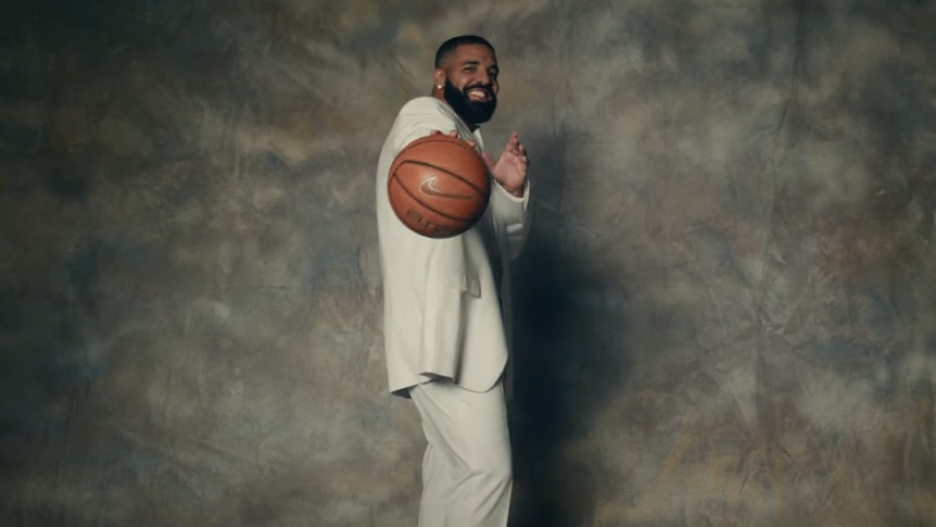 Still of Drake holding a basketball in a beige suit