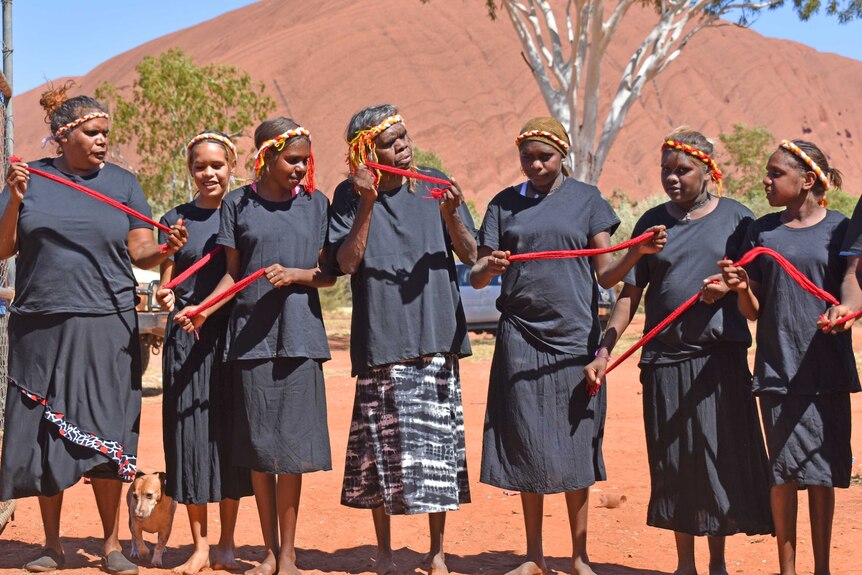 Aboriginal women in community performing a dance in front of Uluru