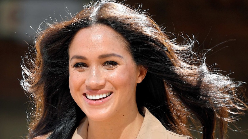 A close up photo of Meghan Markle in bright light with her black hair blowing in the wind.