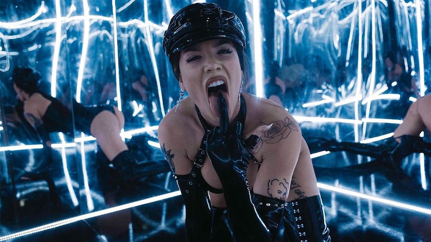 Screenshot from Halsey's music video 'Nightmare' - her dressed in leather, licking her middle finger in room of mirrors