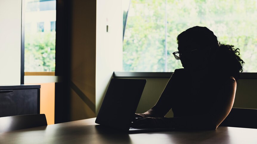 A silhouette of a woman sitting at a table with a laptop.