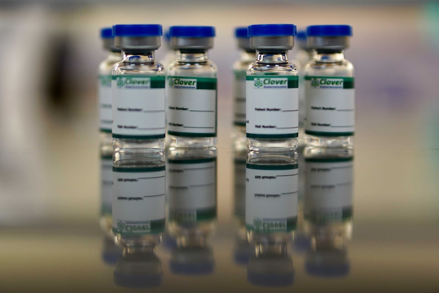 Small glass bottles containing the vaccine are on a metal tray.