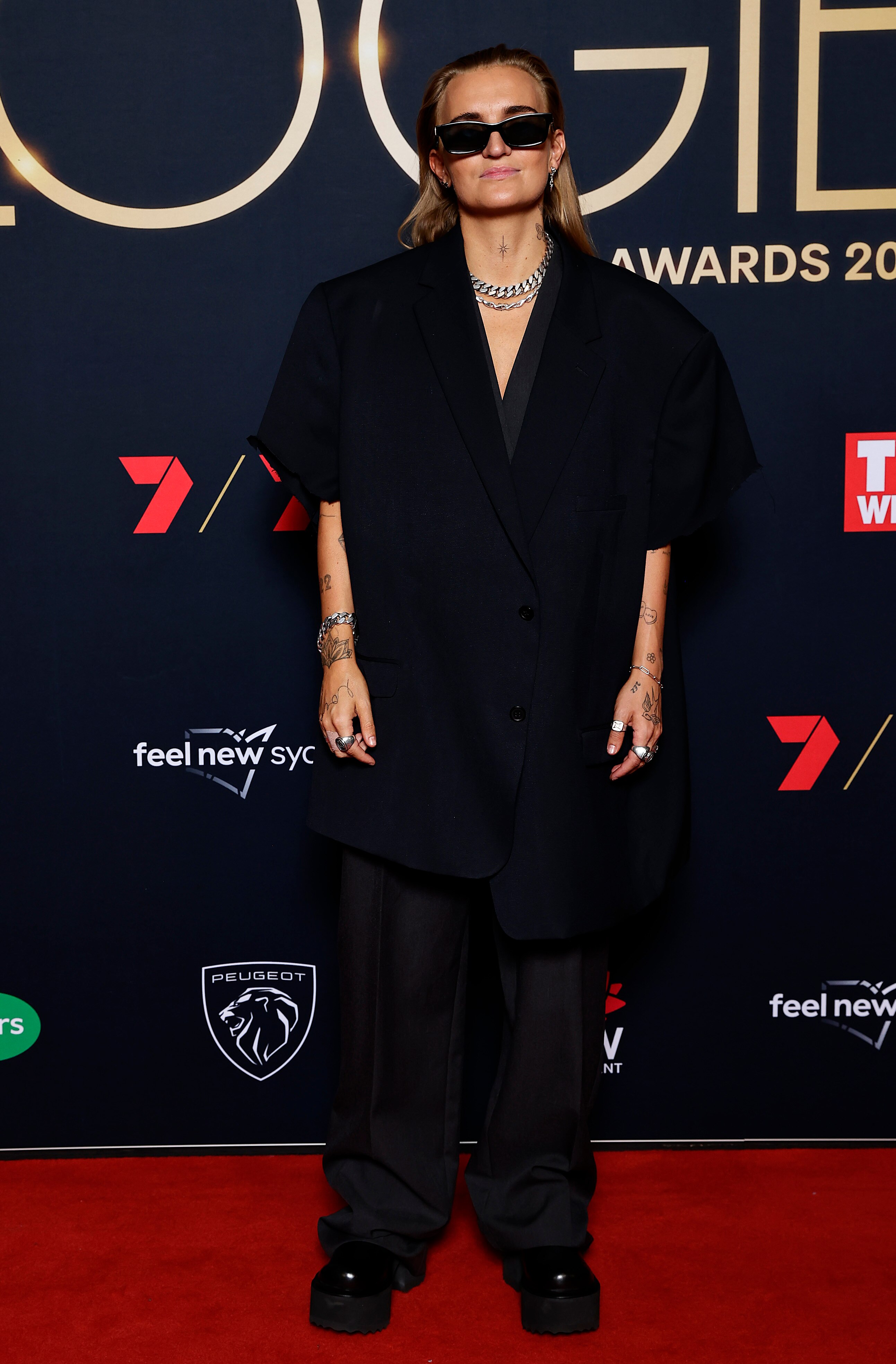 A female musician in a black pants-suit and black shoes with sunglasses on the red carpet