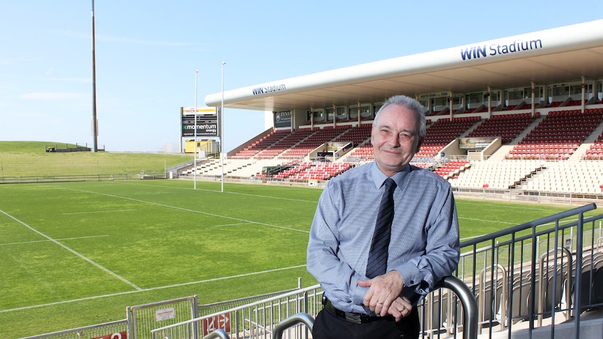Stuart Barnes stands in the western grandstand of WIN Stadium with the football field behind him.