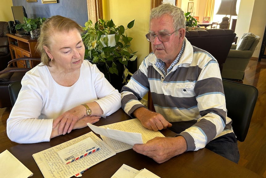Two older people sitting at a table in their home looking at several letters.