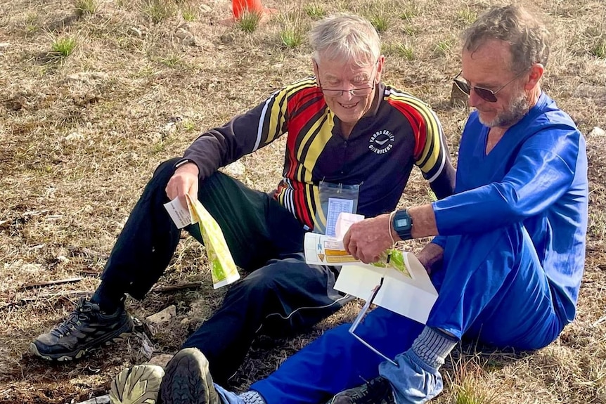 Two men in track suits sitting on the ground looking at piece of paper