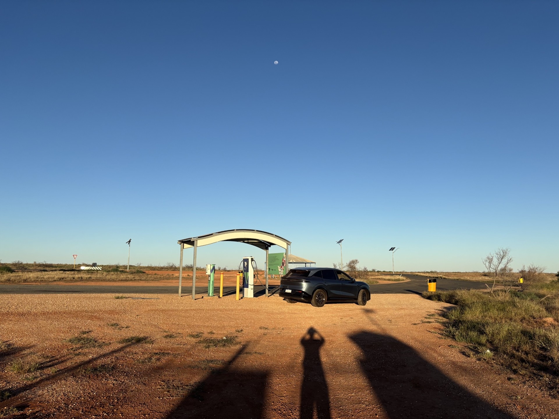 Shadow of photographer in the foreground, as a dark grey electric vehicle sits at a remote curved roof charging station.
