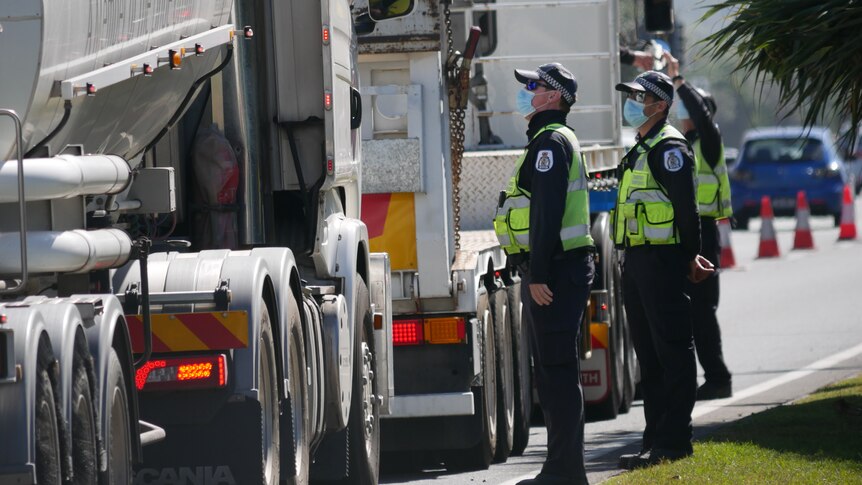 Three police officers wearing masks talk to truck drivers in their vehicles