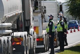 Three police officers wearing masks talk to truck drivers in their vehicles