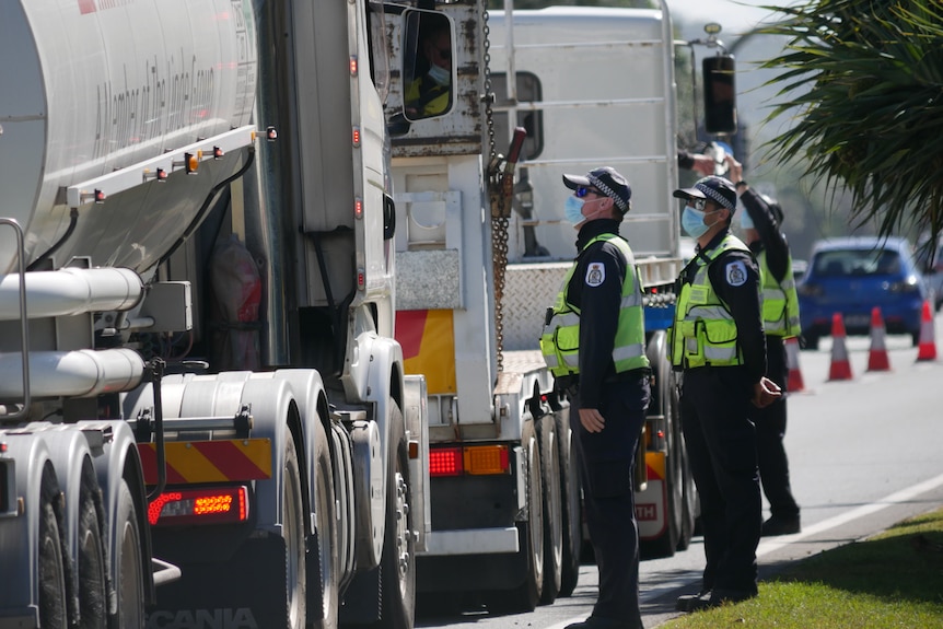 Three police officers wearing masks talk to truck drivers in their vehicles