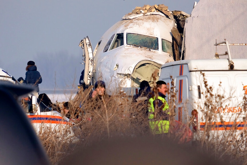The front nose of an airliner is seen smashed next to a building with emergency crews surrounding it.
