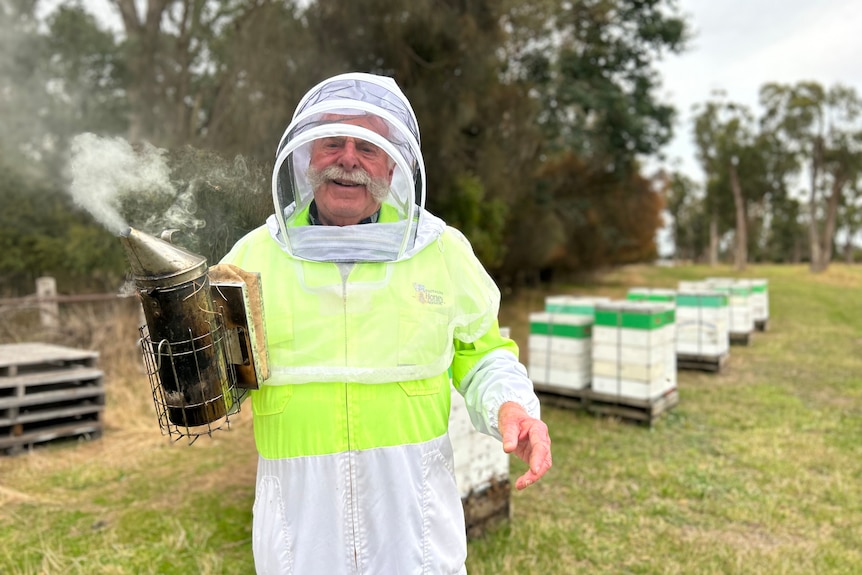 A man in a bee suit holding beekeeping equipment.
