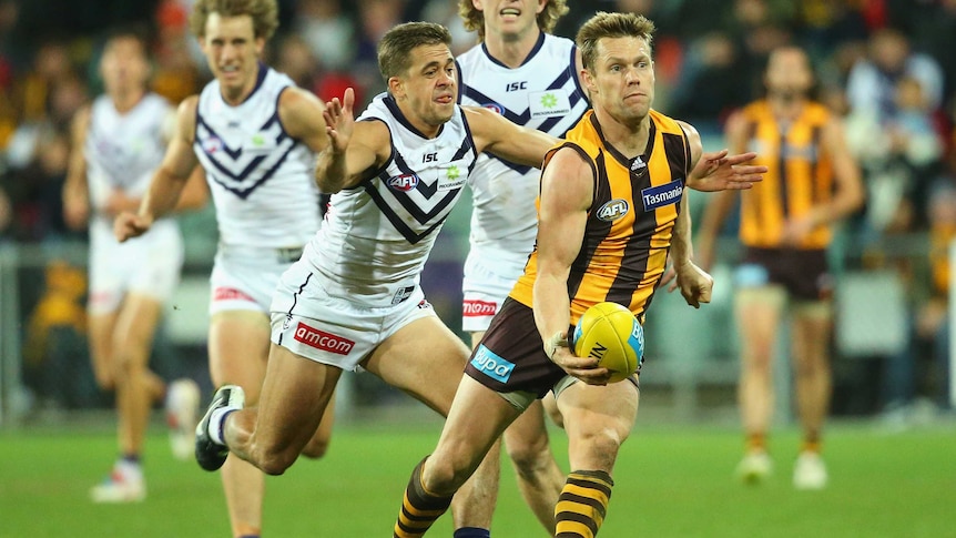 Hawthorn's Sam Mitchell handballs while being tackled by Fremantle's Stephen Hill