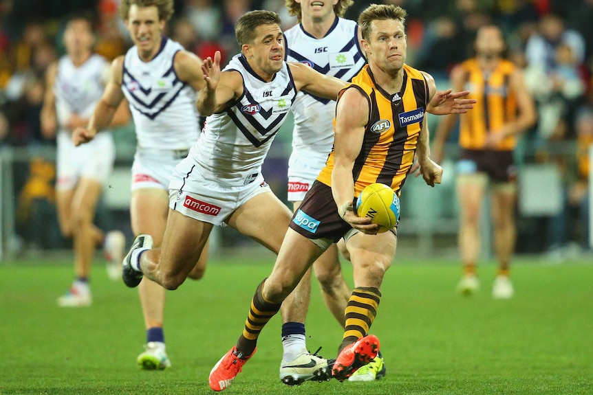 Hawthorn's Sam Mitchell handballs while being tackled by Dockers' Stephen Hill in round 15, 2015.