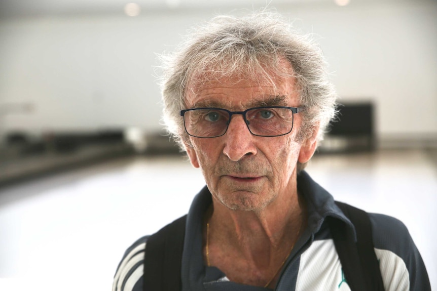 A grey haired man wearing black framed glasses looks into the camera