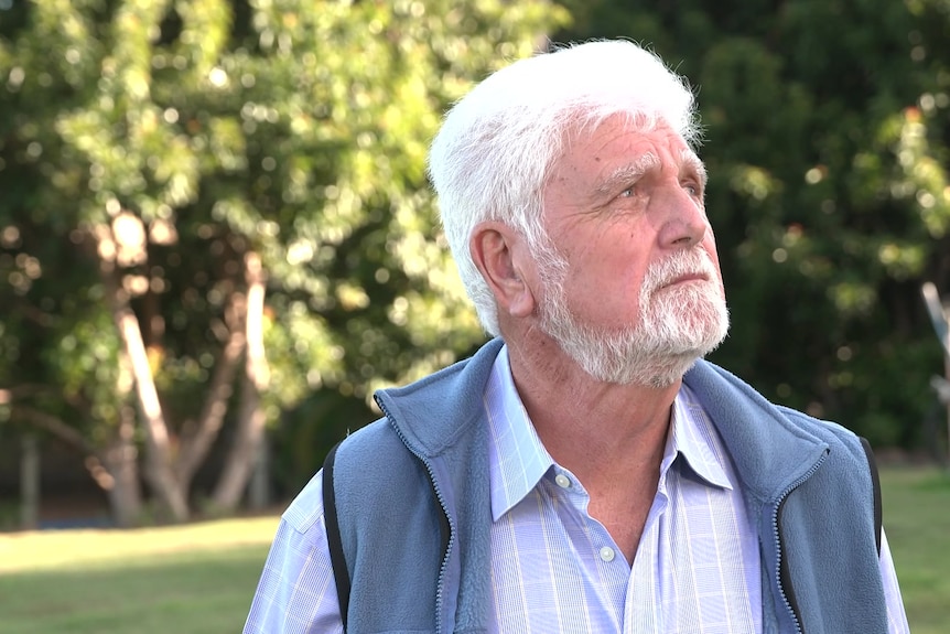 a man with a white hair and a white beard standing outdoors and looking sideways to the left
