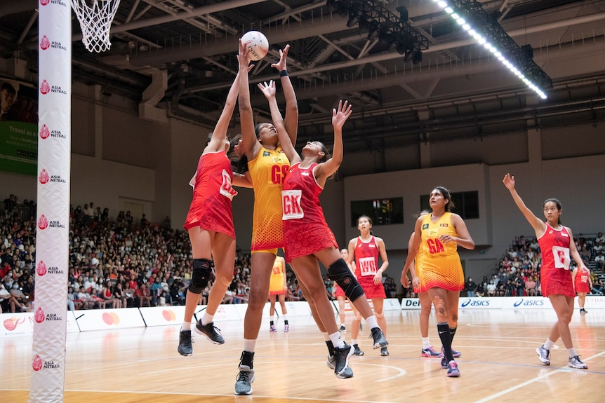Two Singapore defenders and one Sri Lanka goal shooter jump for the ball under the ring.