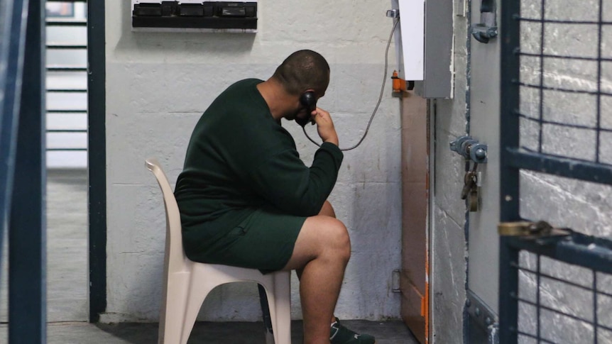 An inmate sits on a chair talking on a landline telephone.