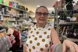 A woman in a white dress with dotes stands in a shop.