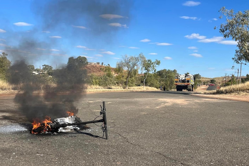 An e-scooter on its side on fire on a road in Marble Bar