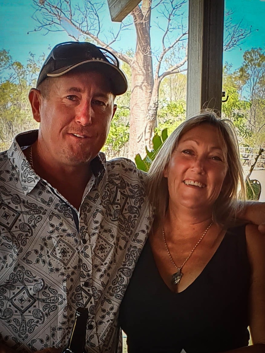 A man and a woman stand smiling at the camera with bush in the background.