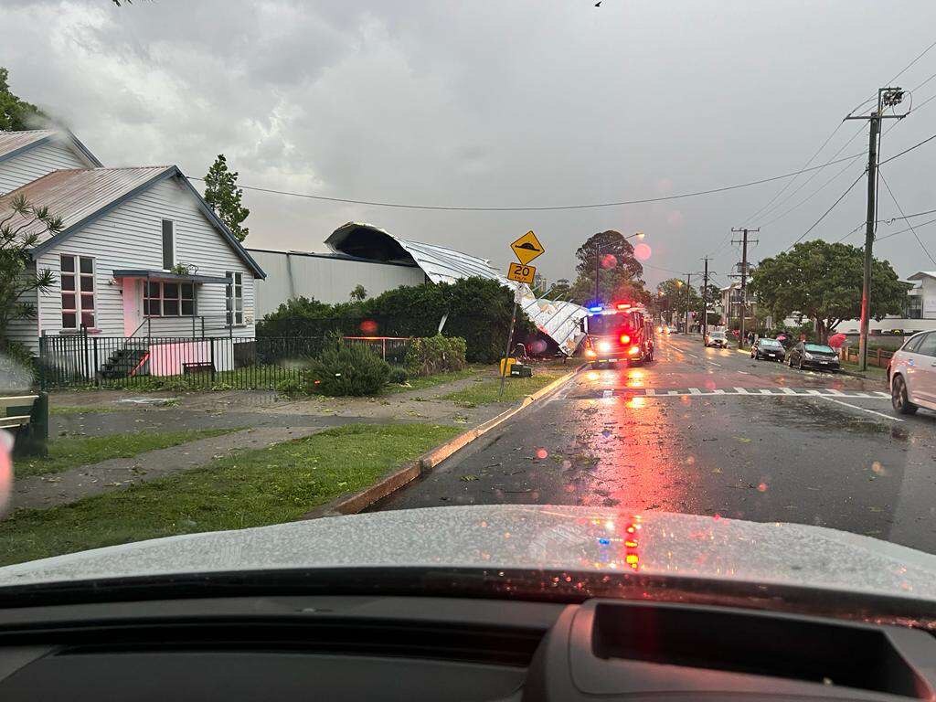 A tin roof falling off the top of a building next to a fire truck. 