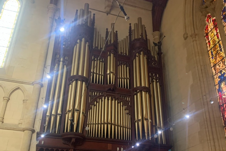 Large pipes from a pipe organ on the wall of a cathedral. To the side is a stained glass window.