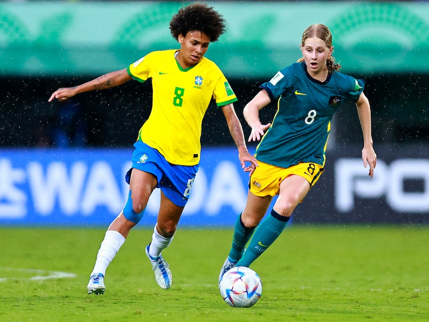 Two female soccer players, one in yellow and blue and another in green and yellow, during a game
