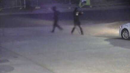 Two men, one of whom is raising a shotgun, running away from the service station.