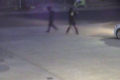 Two men, one of whom is raising a shotgun, running away from the service station.