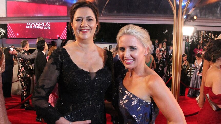 Annastacia Palaszczuk and Kate Jones smiling at the camera wearing formal gowns on a red carpet.