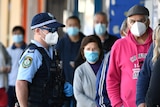 Members of the public wearing face masks queue outside a bank as a police officer watches. 