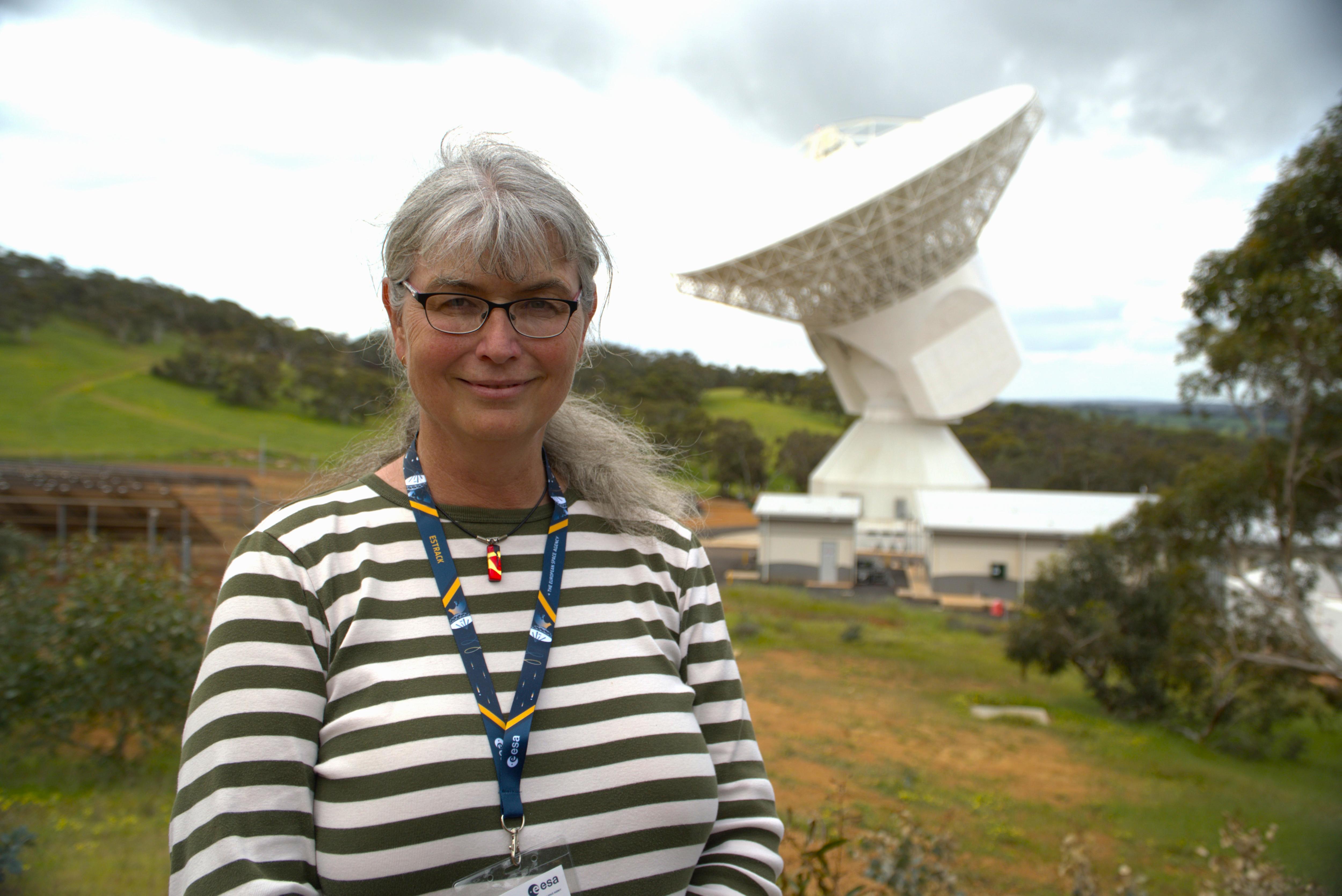 Suzy Jackson wears a striped shirt and smiles as she stands in front of a large satellite dish.