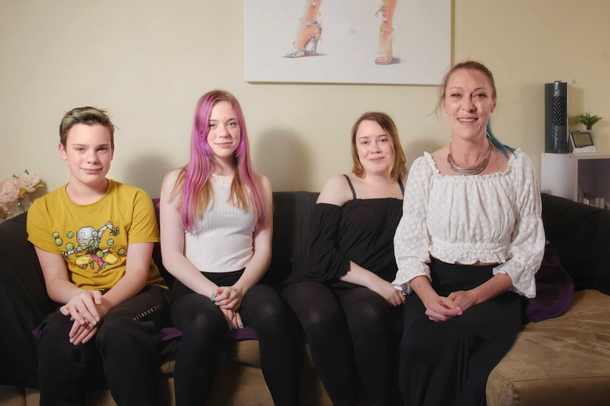 a family sits side by side on a couch, smiling at the camera