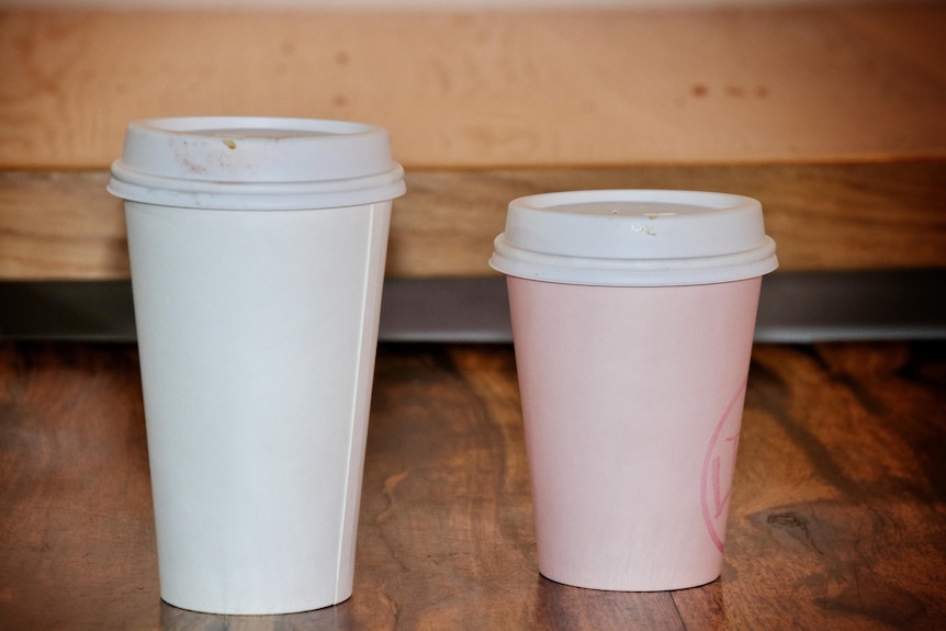 A large and small takeaway coffee cup side by side on a wooden counter.