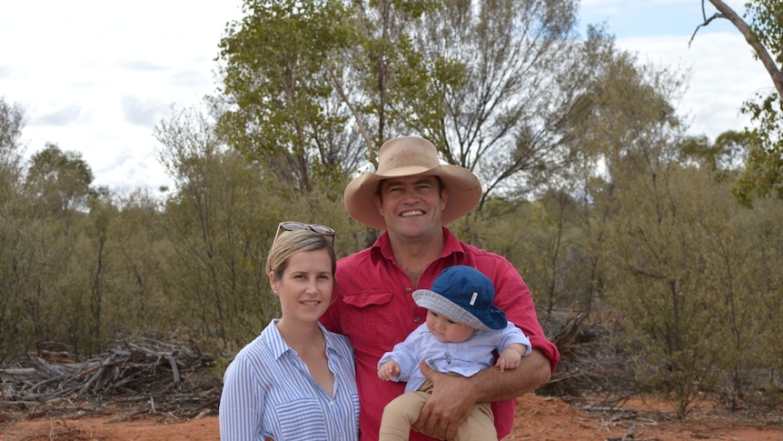 A couple stand in outback Queensland holding their baby
