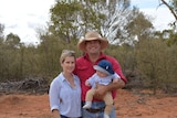 A couple stand in outback Queensland holding their baby