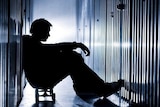 Silhouette of young man seated on a skateboard in a narrow, metal lined corridor