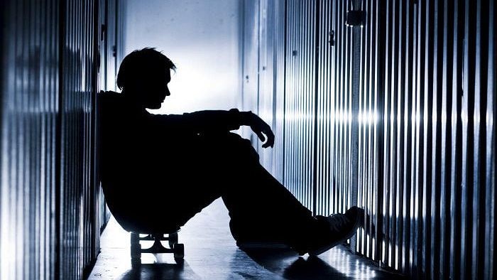 Silhouette of young man seated on a skateboard in a narrow, metal lined corridor