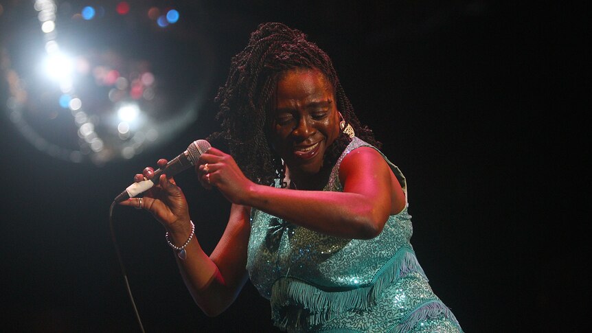 Sharon Jones dances on stage, wearing a bright green sparkly dress