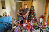 A man and woman stand next to a Christmas tree surrounded by children's bikes